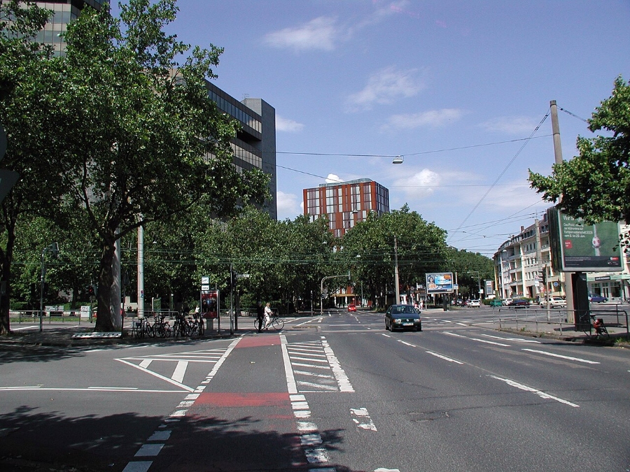 Aachener Straße in Cologne, featuring a car driving along the street amidst urban scenery.
