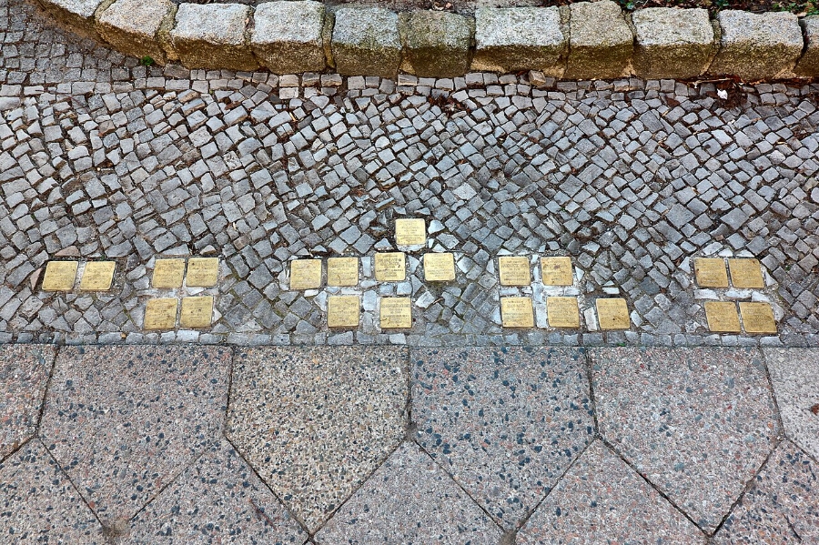 Close-up of Stolpersteine, small gold plaques embedded in a sidewalk, honoring Holocaust victims in Berlin, Germany.
