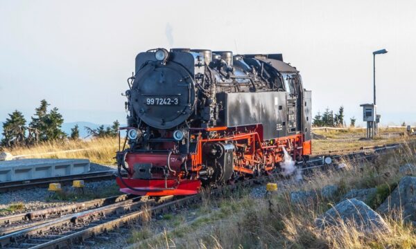 Vintage steam locomotive on railway tracks surrounded by lush countryside scenery.