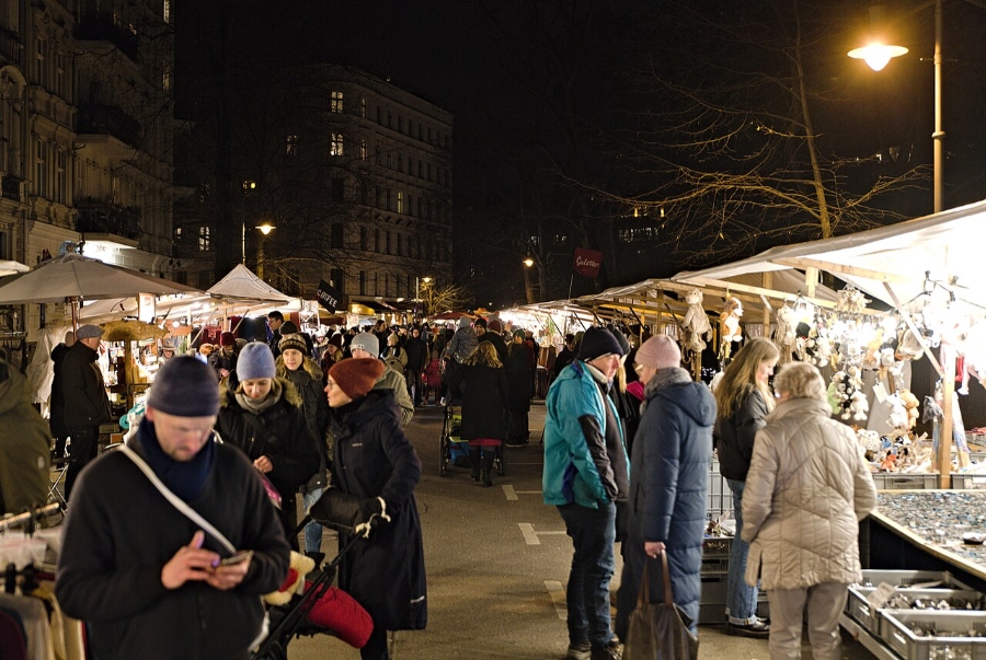 German Christmas Traditions: A Complete Guide 33 People shopping at a festive Christmas market in Berlin, illuminated by colorful lights at night.