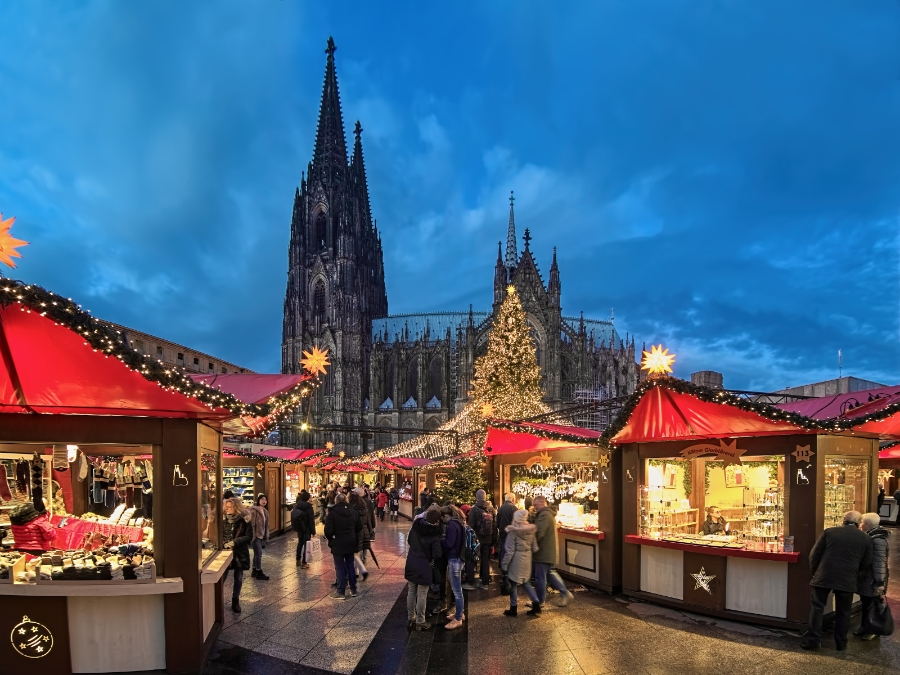 German Christmas Traditions: A Complete Guide 3 Cologne Cathedral illuminated at night, surrounded by festive stalls at the Christmas market, with visitors enjoying the atmosphere.