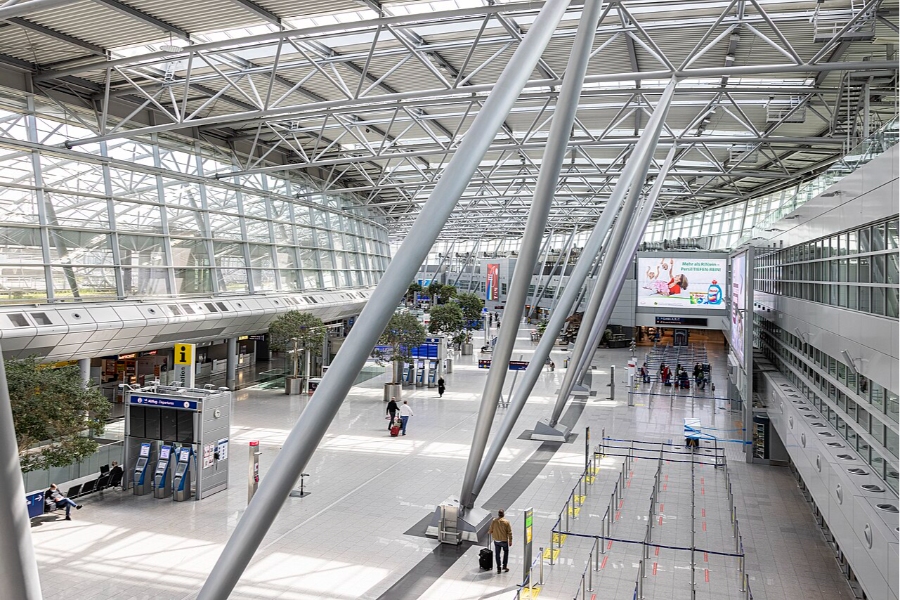 Düsseldorf Airport 4 Interior view of Düsseldorf Airport terminal, featuring numerous passengers, seating areas, and retail spaces.