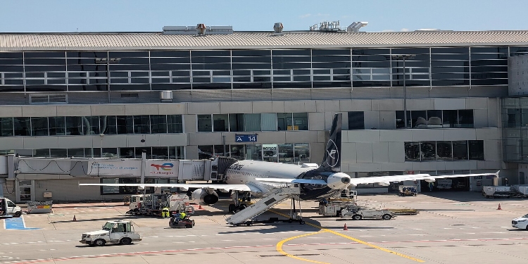 Large white airplane on the tarmac at Frankfurt Airport, surrounded by ground crew and airport infrastructure.