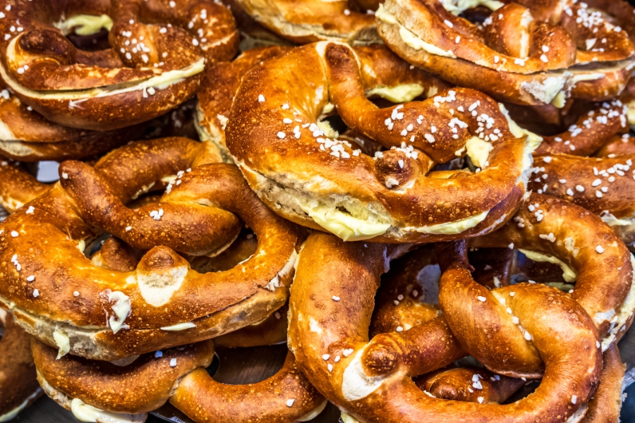 Close-up of a large pile of German pretzels topped with cheese and sesame seeds, showcasing their golden-brown texture.