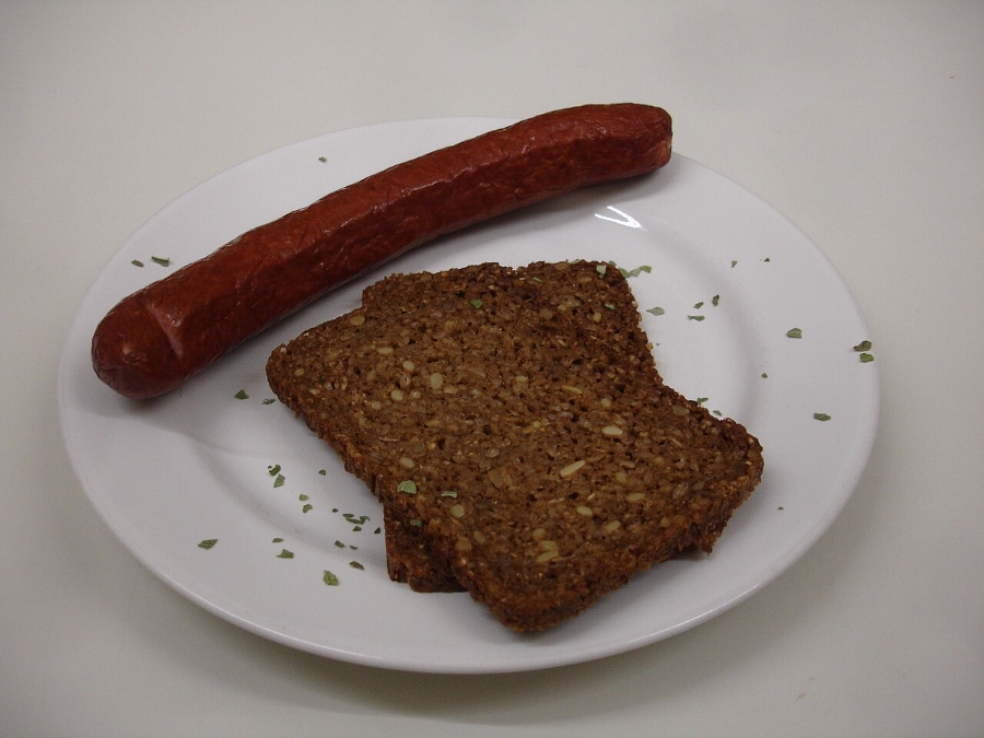 German Bread Culture: Bakeries, Loaves and Traditions 16 Plate featuring a hot dog served with a slice of rye bread, garnished with mustard and onions.