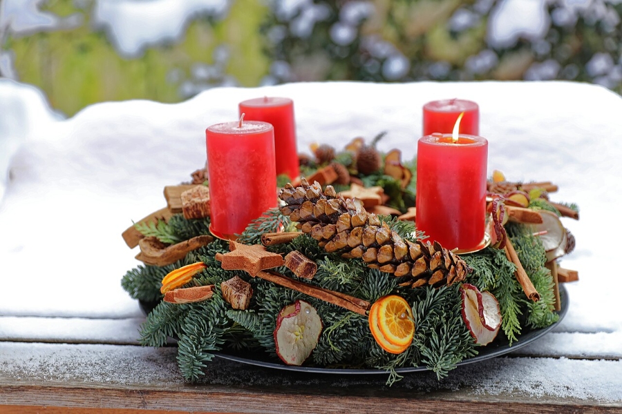 German Christmas Traditions: A Complete Guide 8 Advent wreath with four lit candles and decorative pine cones, placed on a rustic table setting.