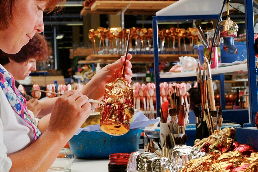 German Christmas Traditions: A Complete Guide 29 Woman carefully crafts a glass ornament in a factory setting, showcasing her skill and attention to detail.