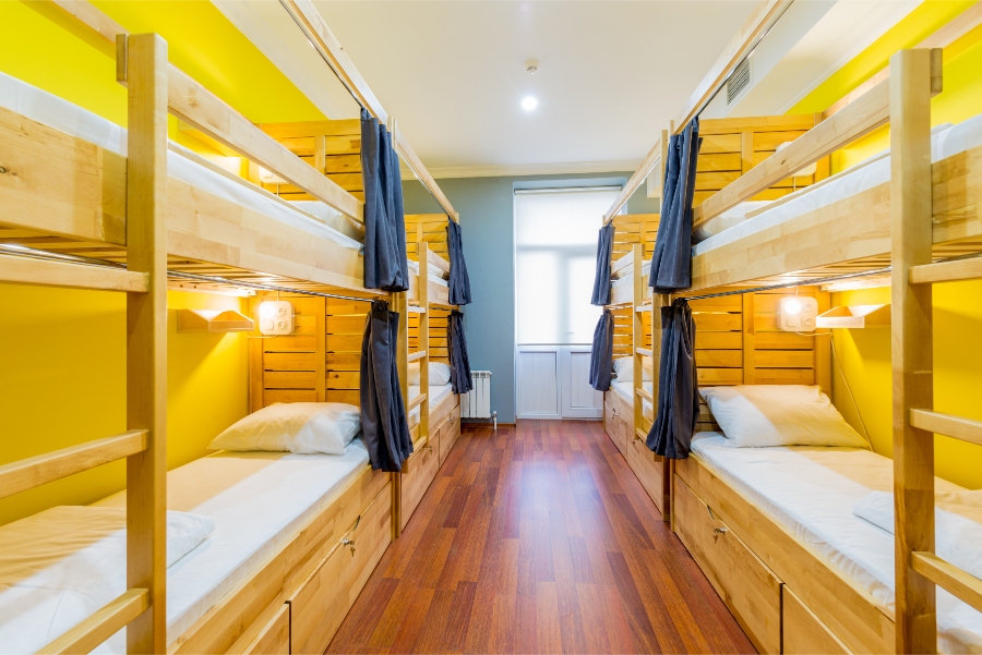 Interior of a hostel dormitory with wooden floors and yellow walls, showcasing several bunk beds for guests.
