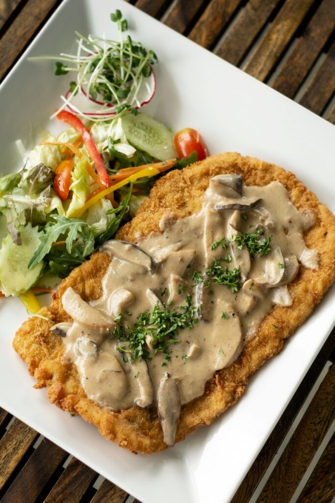 Jagerschnitzel, a veal cutlet in mushroom sauce, served on a plate with a side of vibrant salad.
