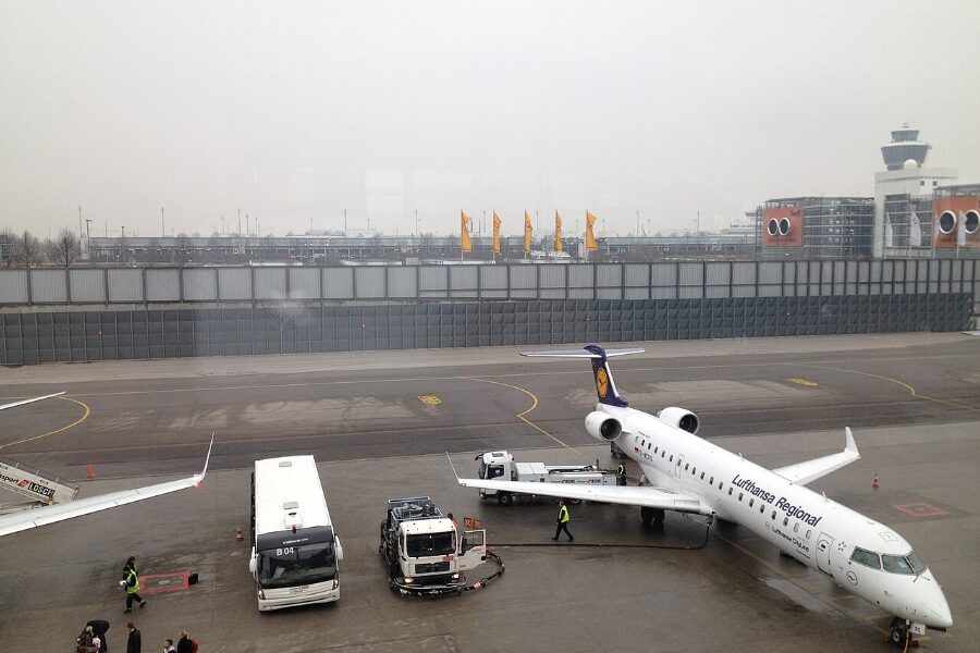 White aircraft stationed on the tarmac at Munich Airport, with a bus and a van in the foreground.