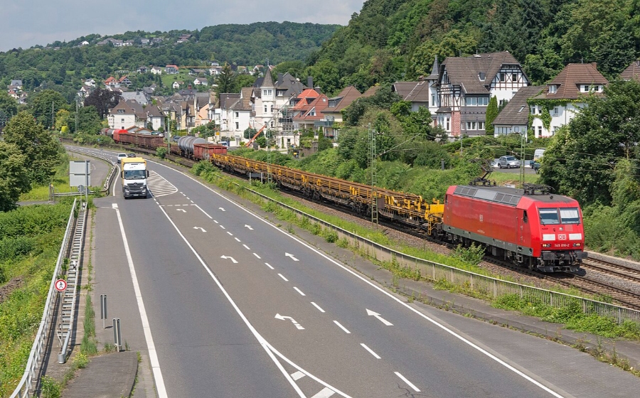 Middle Rhine Valley 18 Train moves down a rural road, accompanied by several cars, highlighting the picturesque setting of Neuwied, Koblenz.