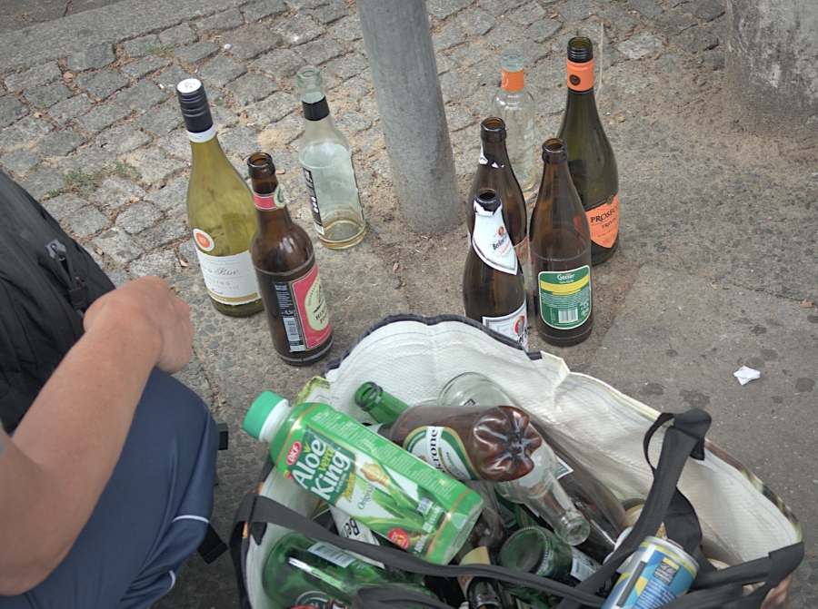 Pfand System Explained: Germany's Bottle Deposit Complete Guide 20 Person collecting recyclable bottles and cans from a street, promoting sustainability and waste reduction efforts.