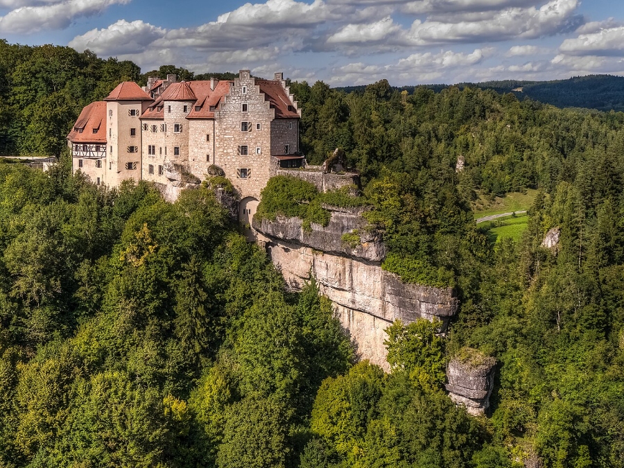 Exploring the German Castle Road: A Complete Guide 10 Aerial view of Rabenstein Castle perched on a cliff, surrounded by lush greenery and a clear blue sky.