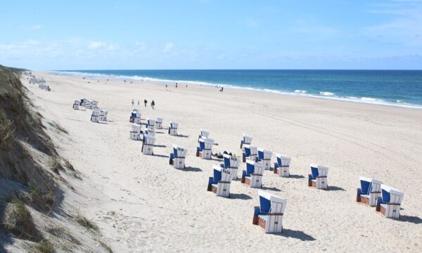 Beach chairs arranged neatly on the sandy beach of Rantum, Sylt, Germany, with gentle waves lapping nearby.