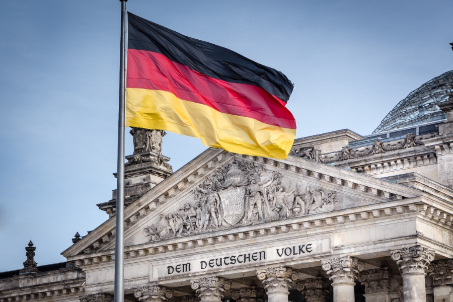 Visiting Germany for the First Time: 20 Essential Tips for New Travelers 13 German flag waving atop the Reichstag Building in Berlin, showcasing its iconic architecture against a clear blue sky.