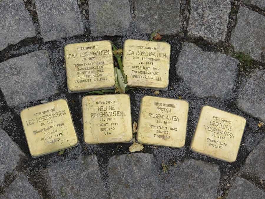 Six gold Stolpersteine plaques arranged in a circle on the ground, commemorating victims of the Holocaust.
