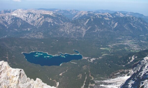 Panoramic view from Zugspitze summit, showcasing mountains and a serene lake below under a clear blue sky.